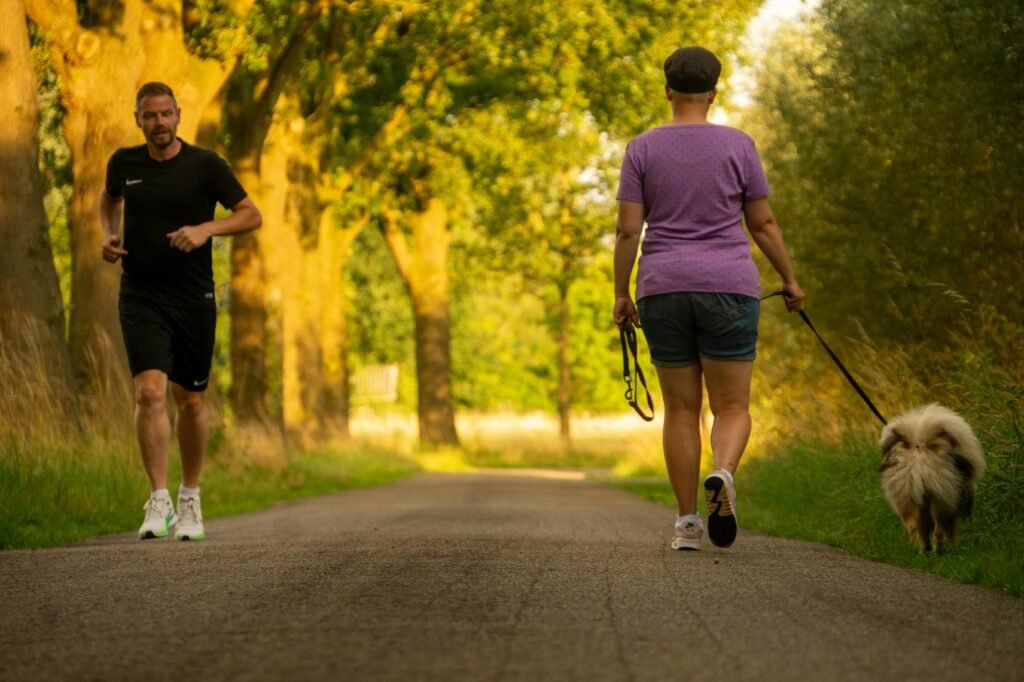 The setting is in a park. A man is jogging (forward facing). A woman is walking her dog (back facing). They are passing each other.