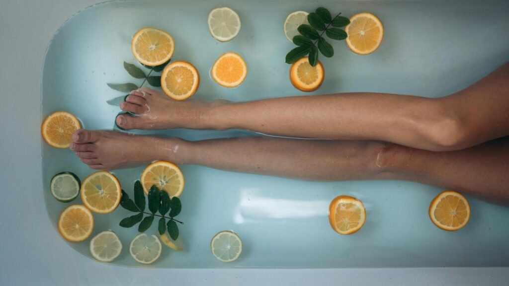 a pair of legs soaking in a bath with orange and lemon slices floating in the water