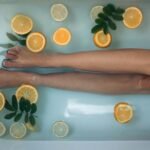 a pair of legs soaking in a bath with orange and lemon slices floating in the water