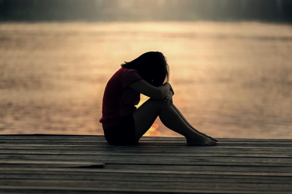 phrases used to manipulate you-a profile of a silhouette figure sitting on sand at the beach with their head on their knees as if covering their face. The lighting is beautiful making it look evening time of day