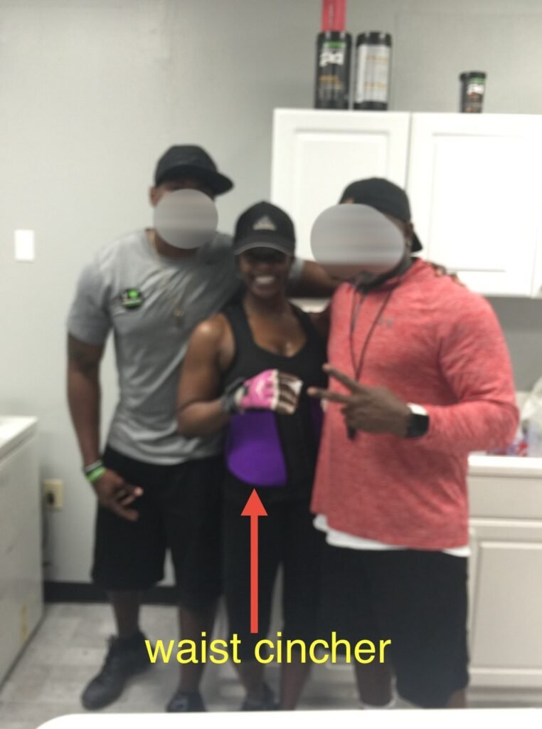 belly fat loss over 40 - the author stands between her 2 personal trainers wearing a purple waist cincher