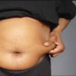 Belly fat loss over 40: an image of a fat belly. Shirt is up and the person is squeezing their belly fat