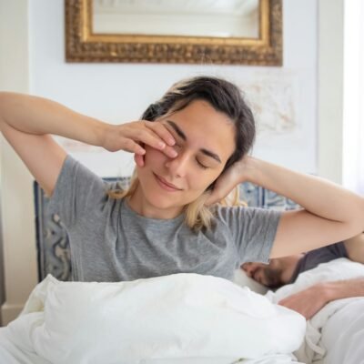 the featured image for this post - a woman waking and sitting up in her bed stretching with arms head level