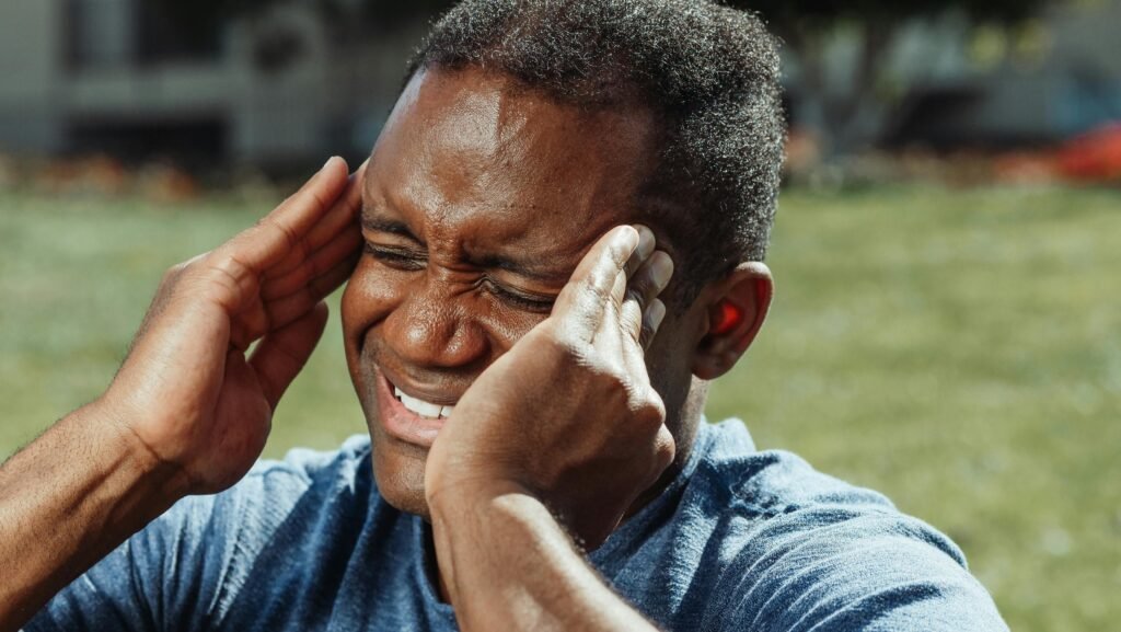 how to detect blood pressure - a young man grimaces in pain with his eyes closed as he rubs his temples signifying a headache or migraine