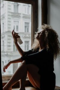 best face mist for hydration -a woman sits on her windowsill misting her face