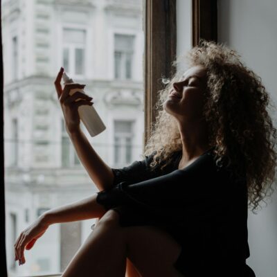 best face mist for hydration -a woman sits on her windowsill misting her face