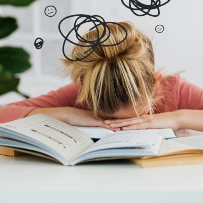 FEATURED IMAGE: get your life together - a woman lays her head down on her desk surrounded by clutter and open books in defeat