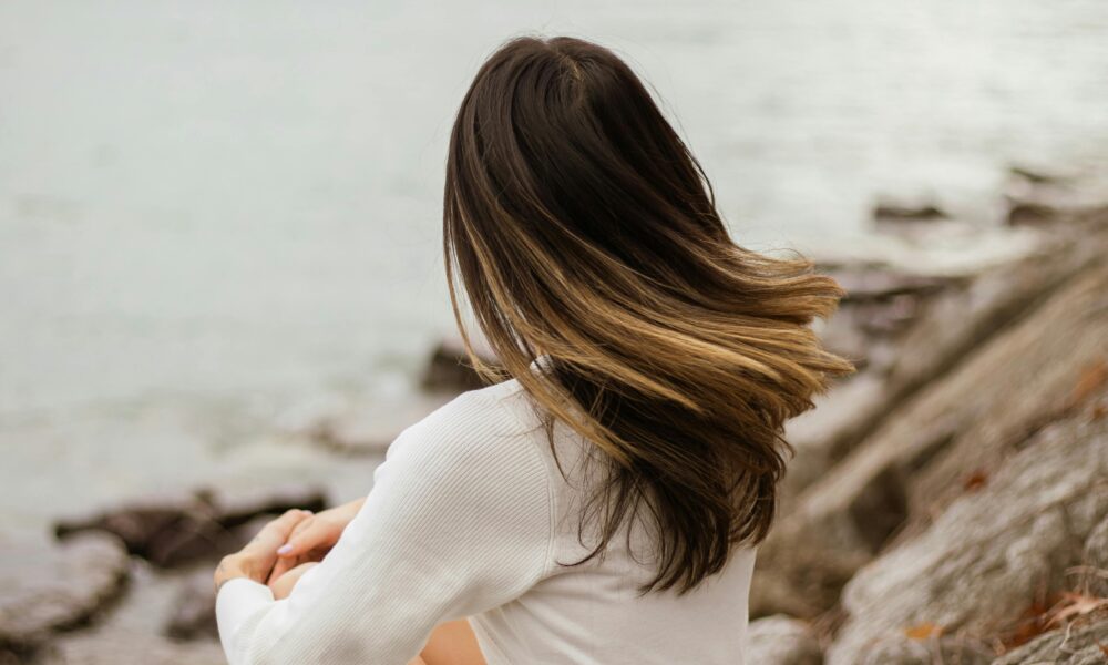 the back of a woman's head as she sits on the sea shore